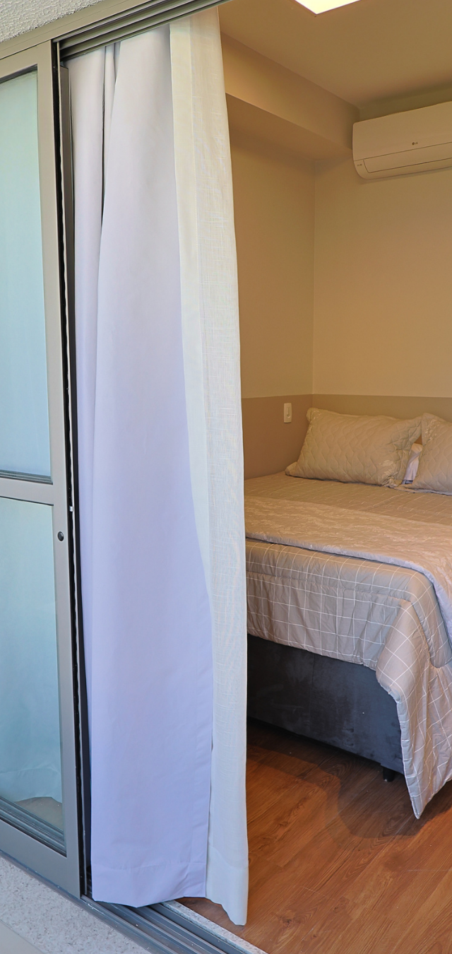 Obra pronta: Cama de casal ao lado da porta de vidro da varanda, com cortina branca e ar-condicionado