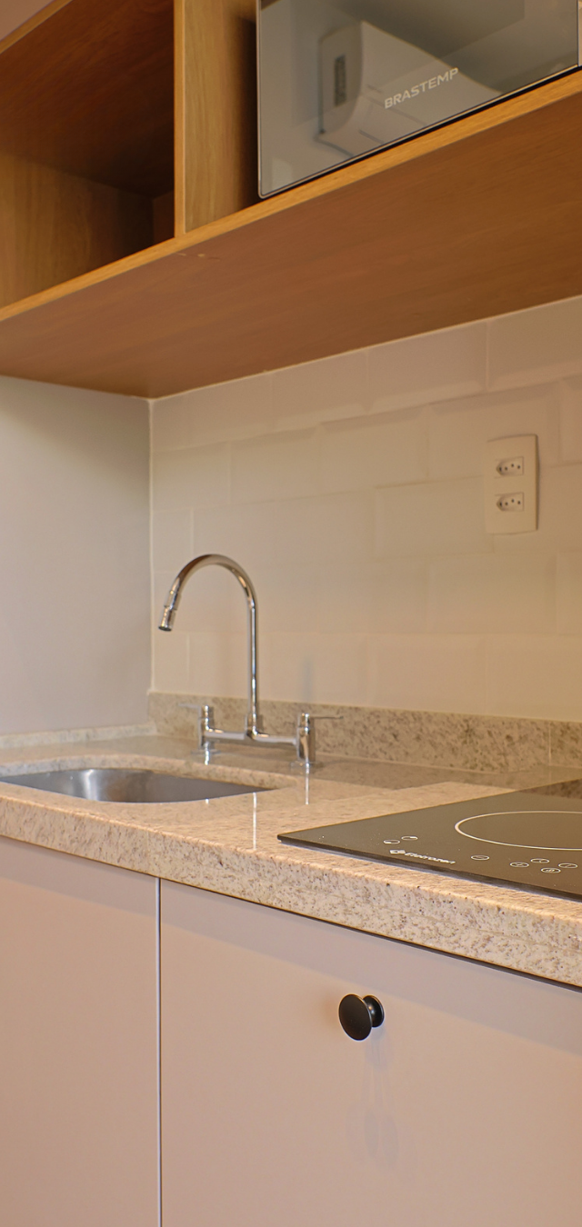 Obra pronta: Pia de cozinha com bancada de granito claro, cooktop de indução e nicho de madeira acima