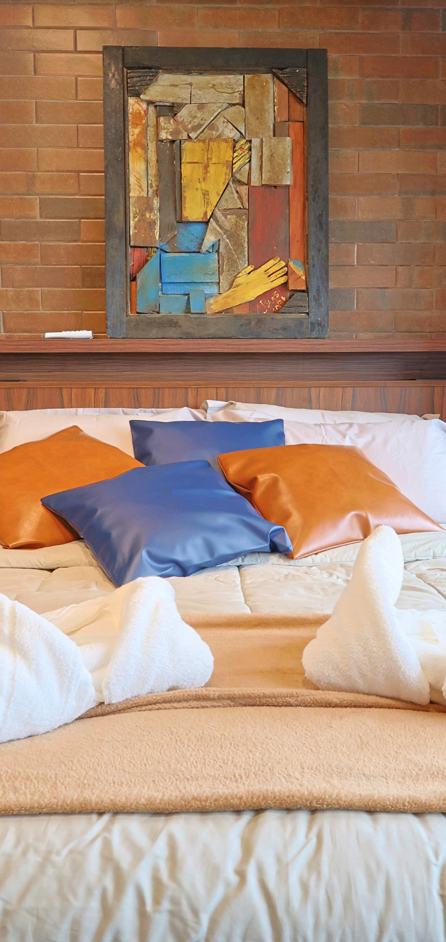 Obra pronta: Cama com almofadas laranja e azuis, toalhas dobradas e quadro colorido na parede de tijolinho