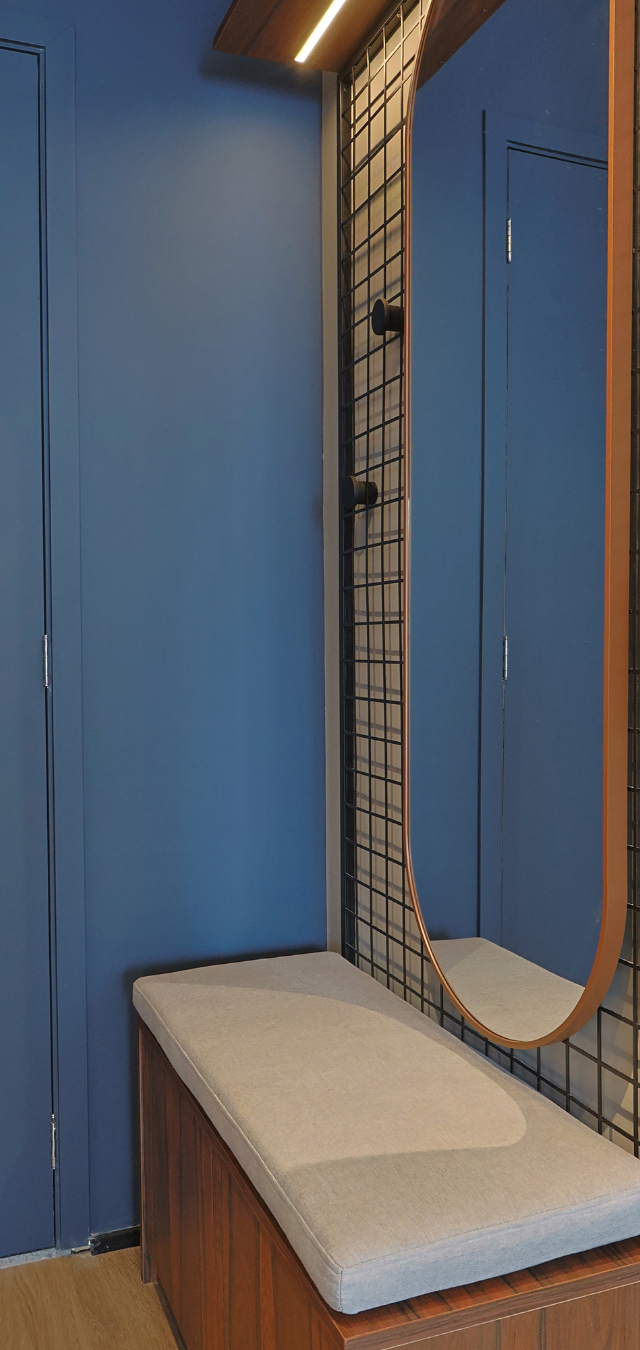 Obra pronta: Banco estofado com espelho oval de moldura de madeira e painel de grade preta, parede azul