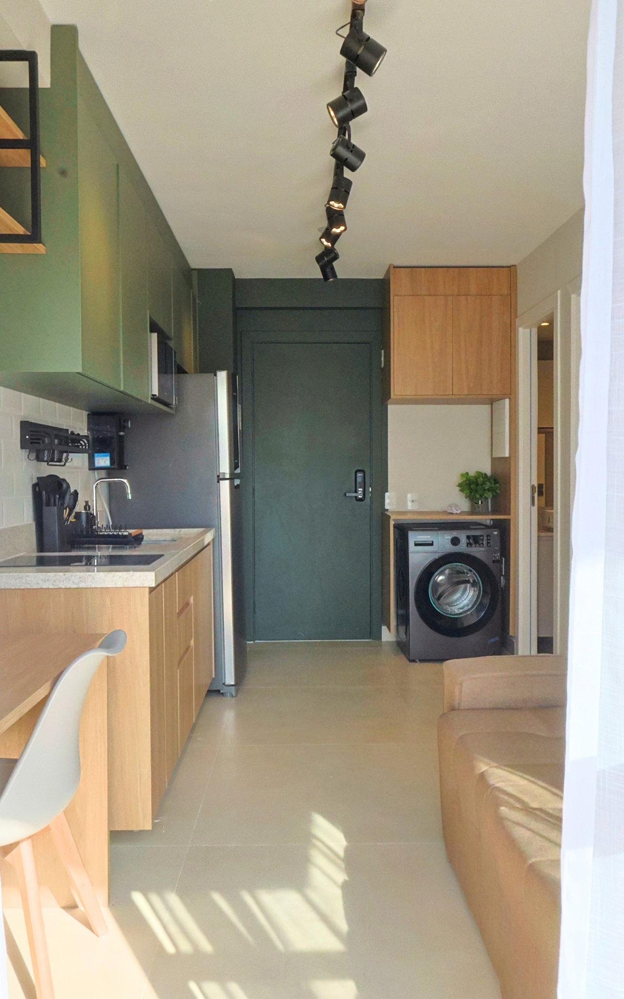 Obra pronta: Cozinha linear verde e madeira, trilho de spots, porta de entrada verde e máquina de lavar ao fundo