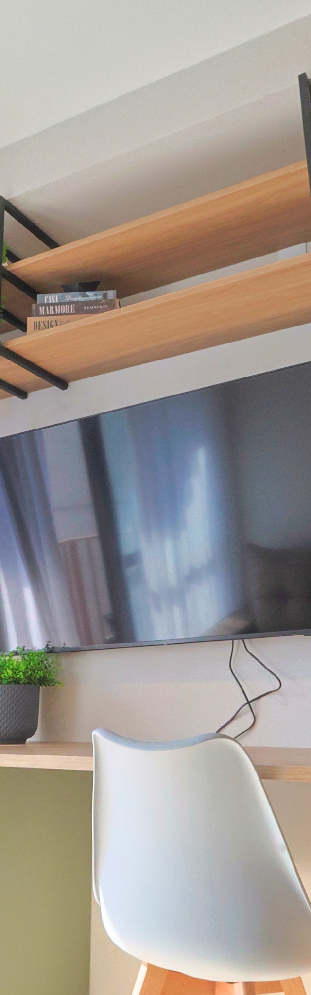 Obra pronta: Mesa de trabalho com cadeira branca, TV na parede e prateleiras de madeira com planta