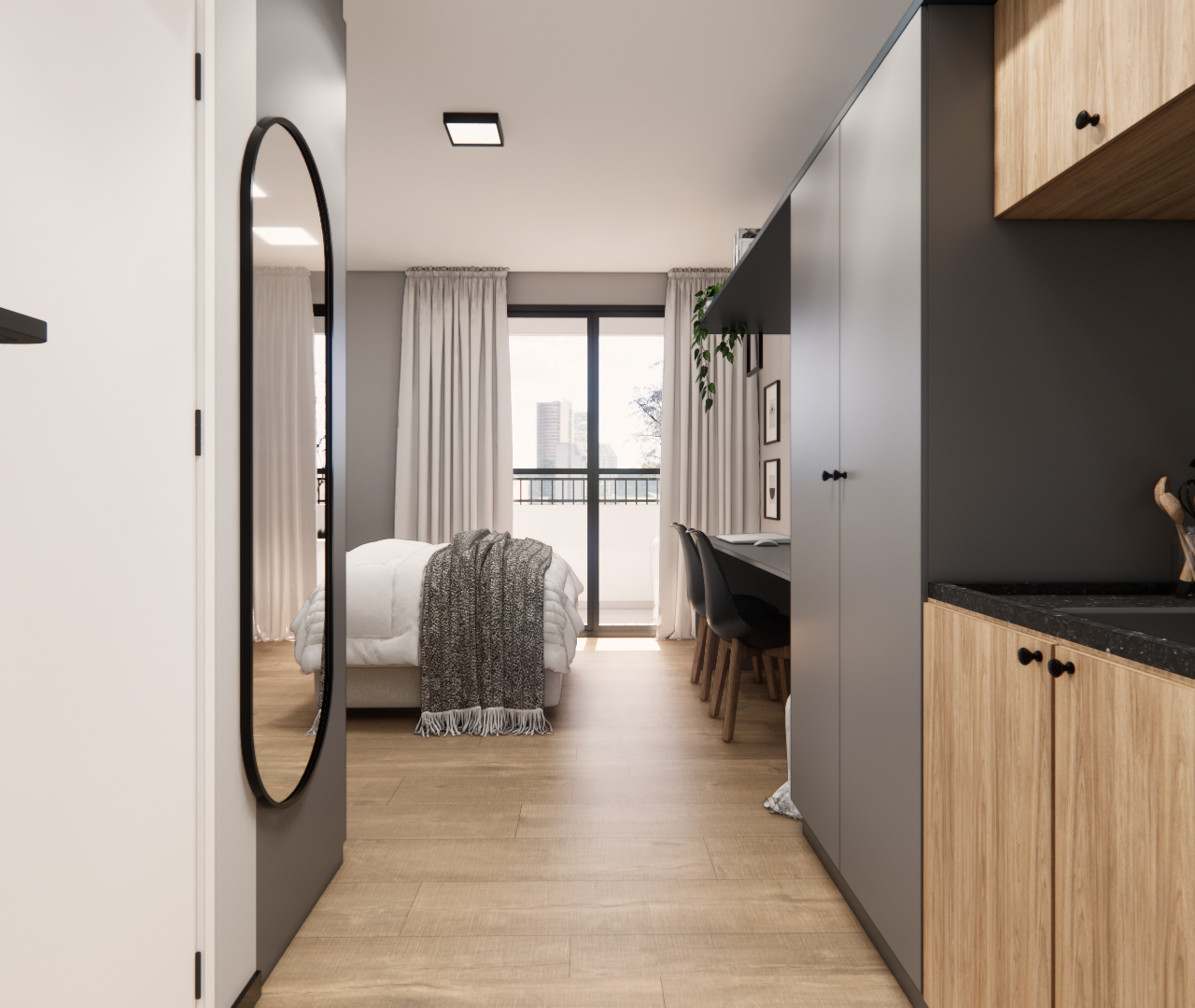 Passagem entre cozinha amadeirada e armários cinza, com bancada preta, espelho vertical e cama ao fundo do ambiente.