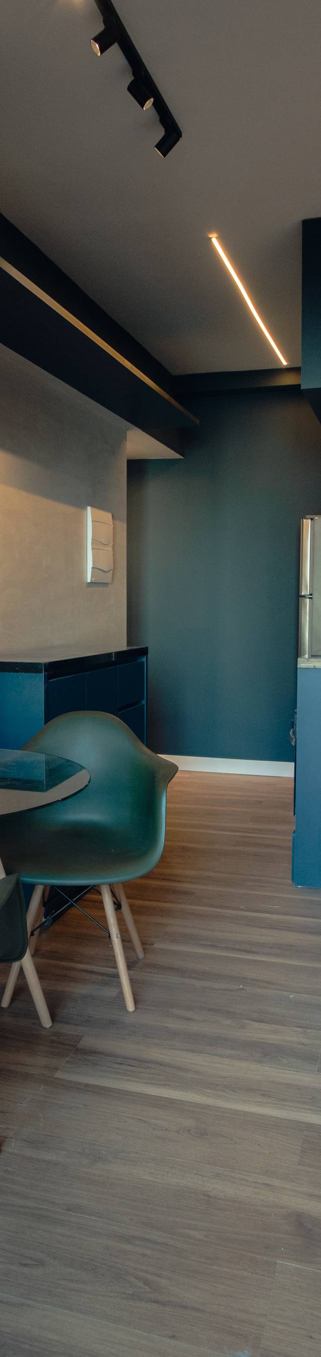 Obra pronta: Studio com mesa redonda de vidro, cadeiras verdes, cozinha em azul-petróleo e cama em primeiro plano