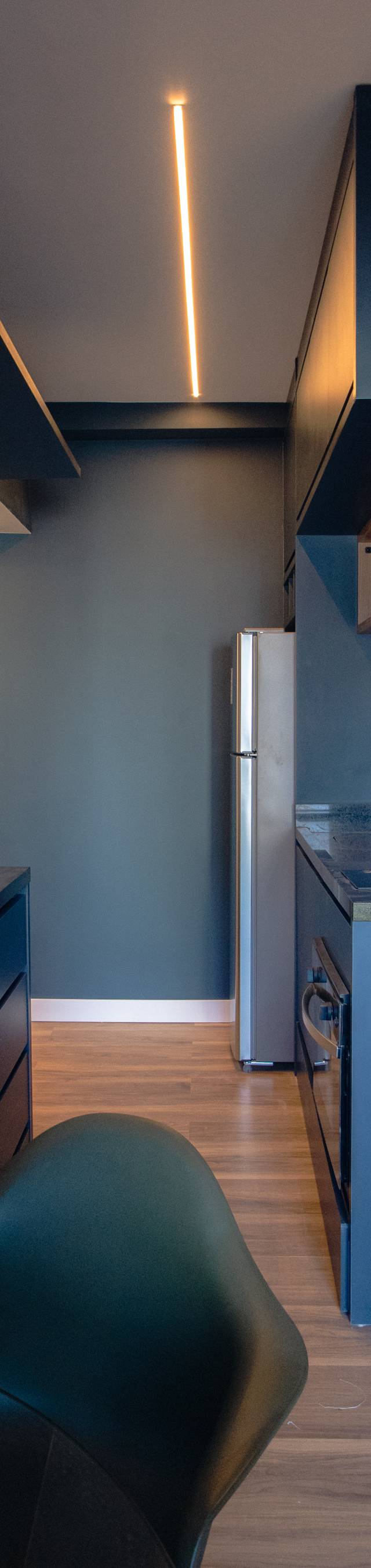 Obra pronta: Cozinha linear em azul-petróleo com geladeira inox, bancada escura e perfil de luz no teto