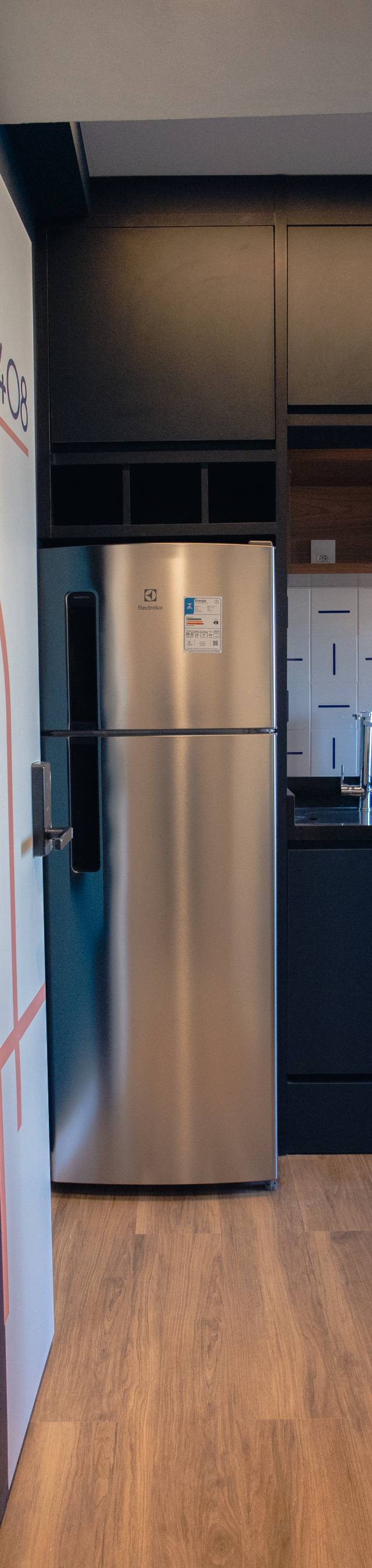Obra pronta: Entrada do studio com porta grafitada e cozinha azul-escura com geladeira inox ao fundo