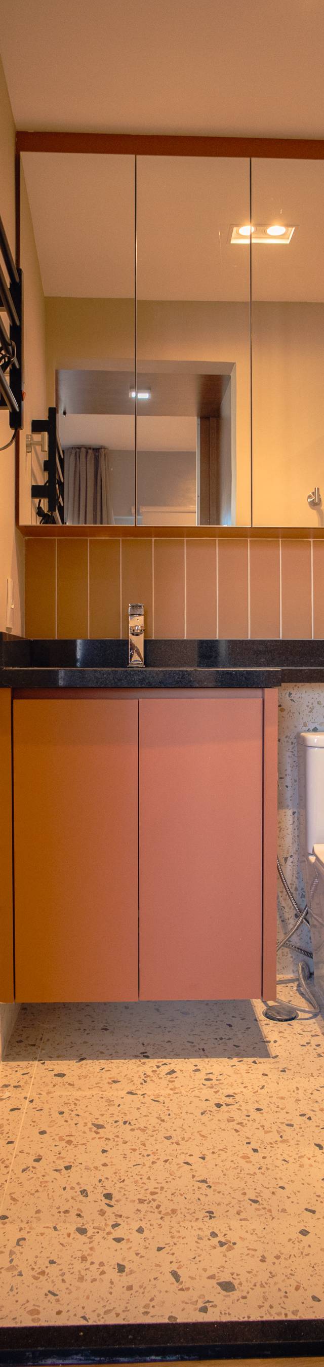 Obra pronta: Banheiro com gabinete terracota, espelho, revestimento laranja e piso granilite, visto pela porta