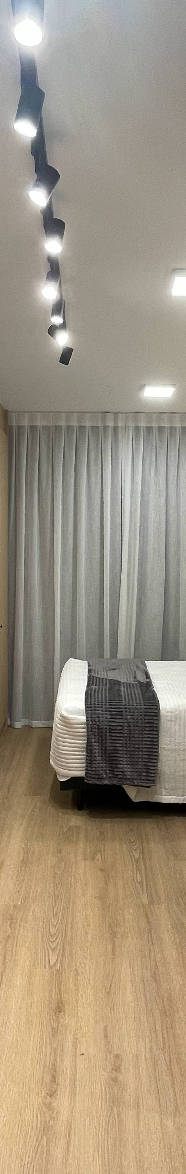 Obra pronta: Studio com cozinha de madeira clara e geladeira inox, trilho de spots e cama ao fundo