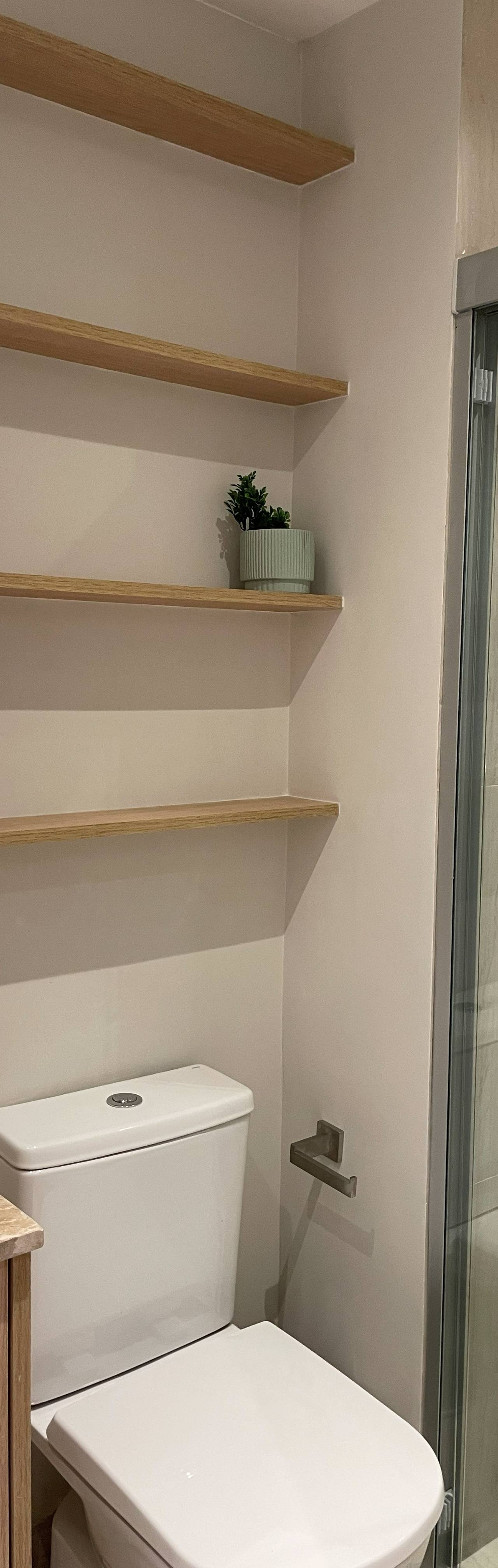 Obra pronta: Banheiro com prateleiras de madeira, vaso sanitário e box de vidro com revestimento bege