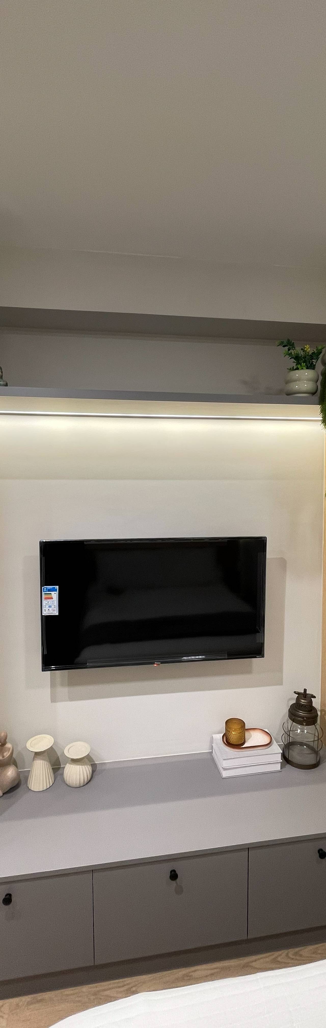 Obra pronta: Painel de TV entre armários de madeira clara, prateleira com planta e aparador cinza
