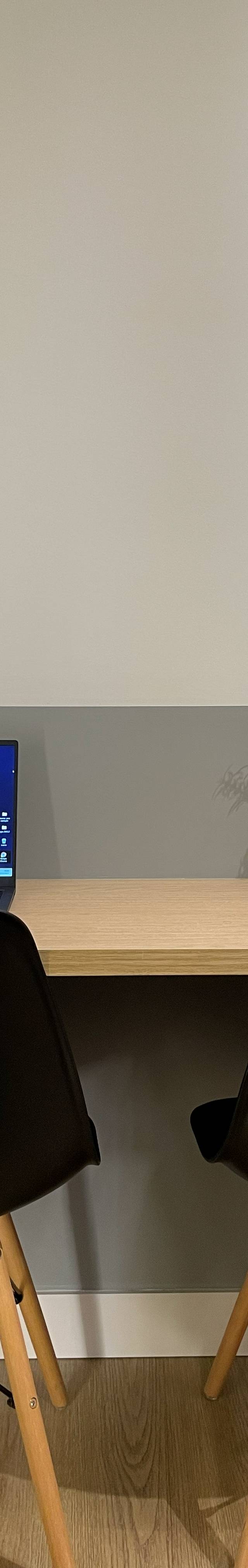 Obra pronta: Bancada de trabalho de madeira com duas cadeiras pretas, notebook e meia-parede cinza