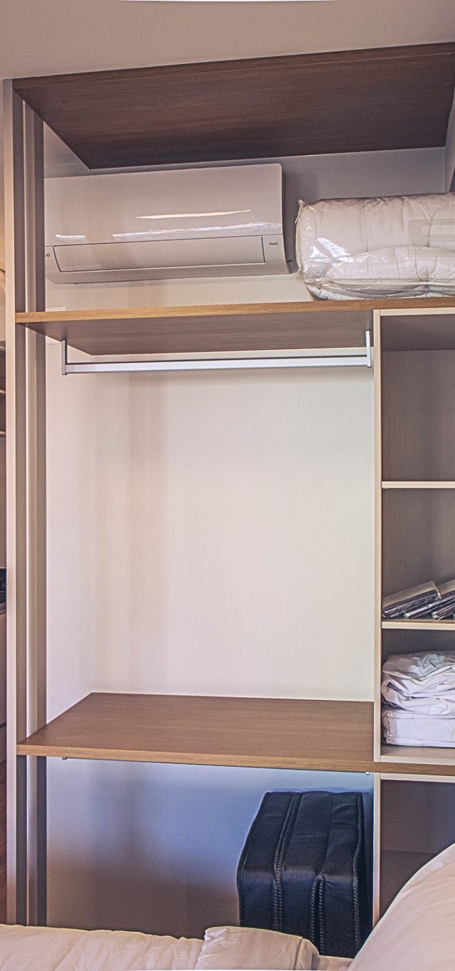 Obra pronta: Estante aberta com cabideiro e enxoval dobrado, com a cozinha e a geladeira inox ao fundo