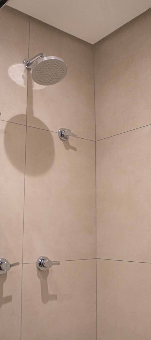 Obra pronta: Interior do box com chuveiro de teto e revestimento bege em placas grandes