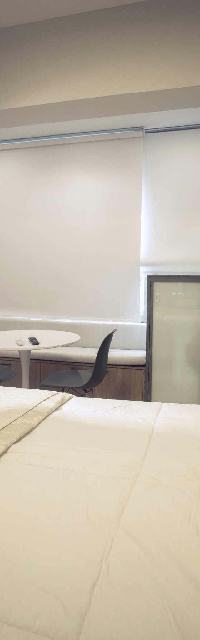 Obra pronta: Cama de casal com mesa redonda branca, cadeiras e banco estofado junto à janela com persiana