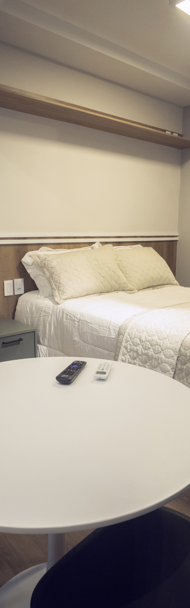 Obra pronta: Mesa redonda branca em primeiro plano e cama de casal com cabeceira de madeira e espelho