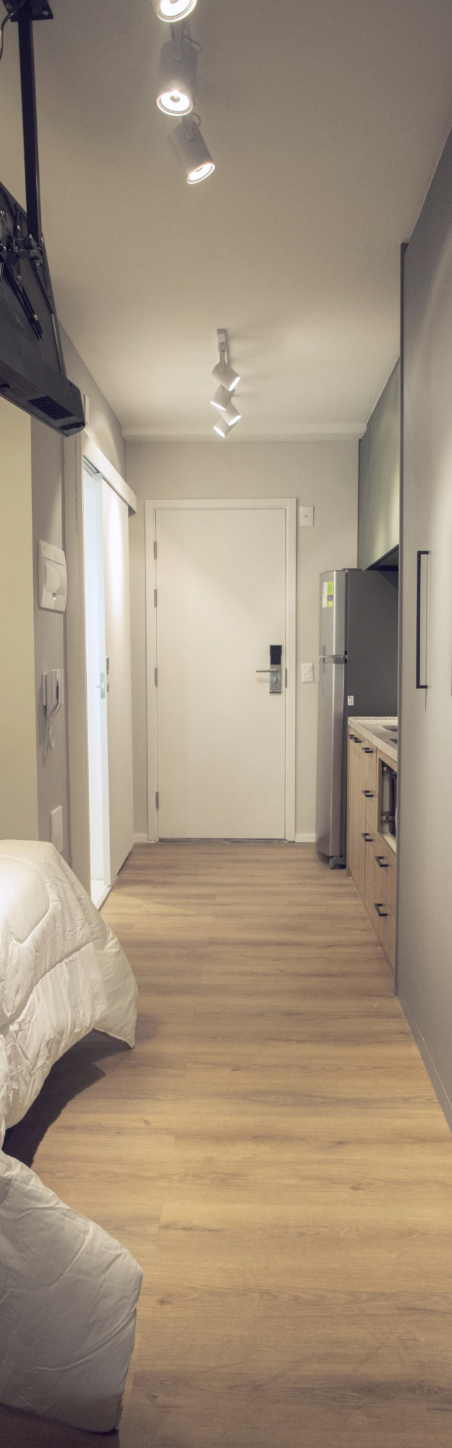 Obra pronta: Studio com cama de casal, armários cinza do piso ao teto, TV no suporte e porta de entrada