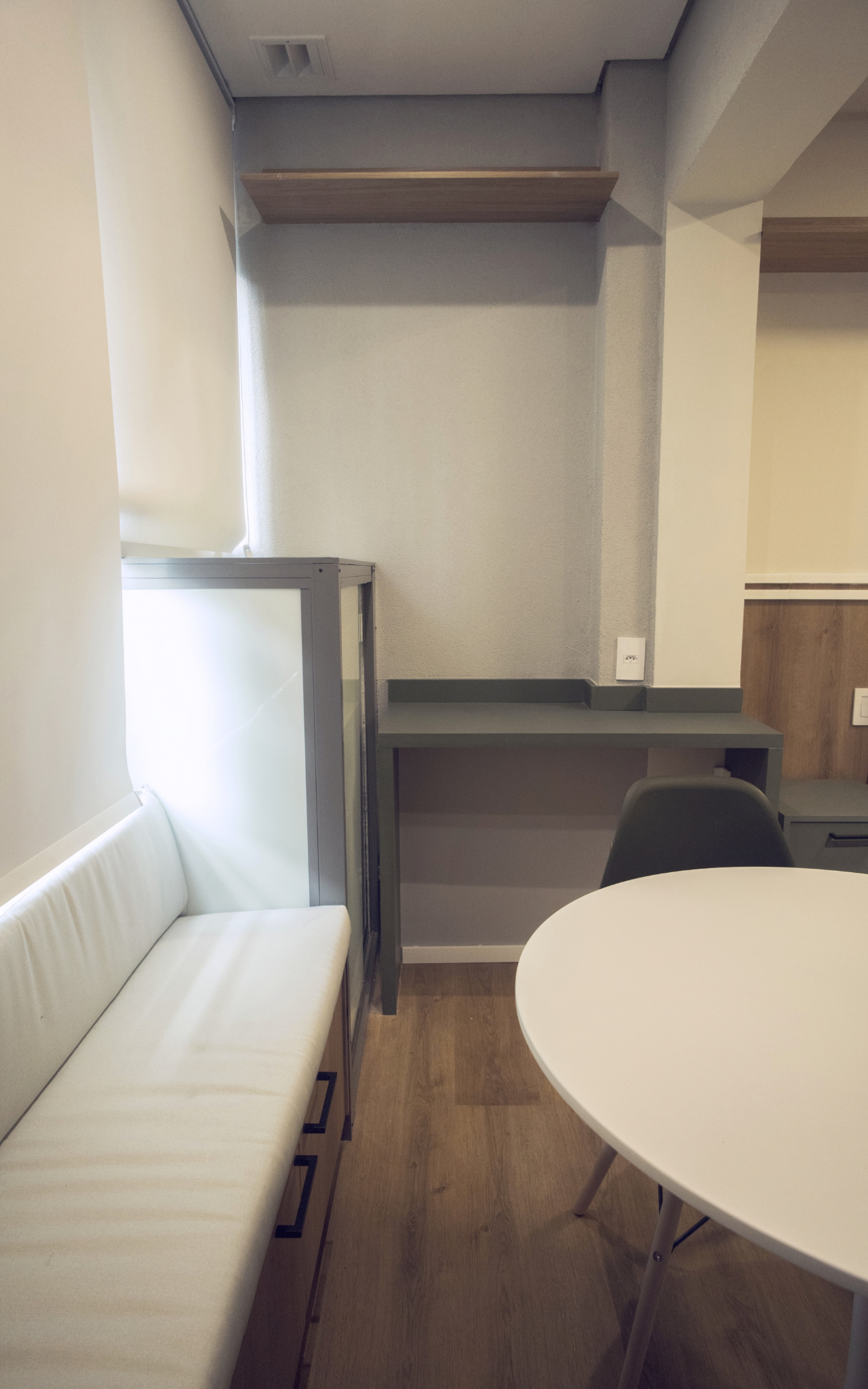 Obra pronta: Banco estofado branco, mesa redonda e bancada cinza junto à janela com persiana