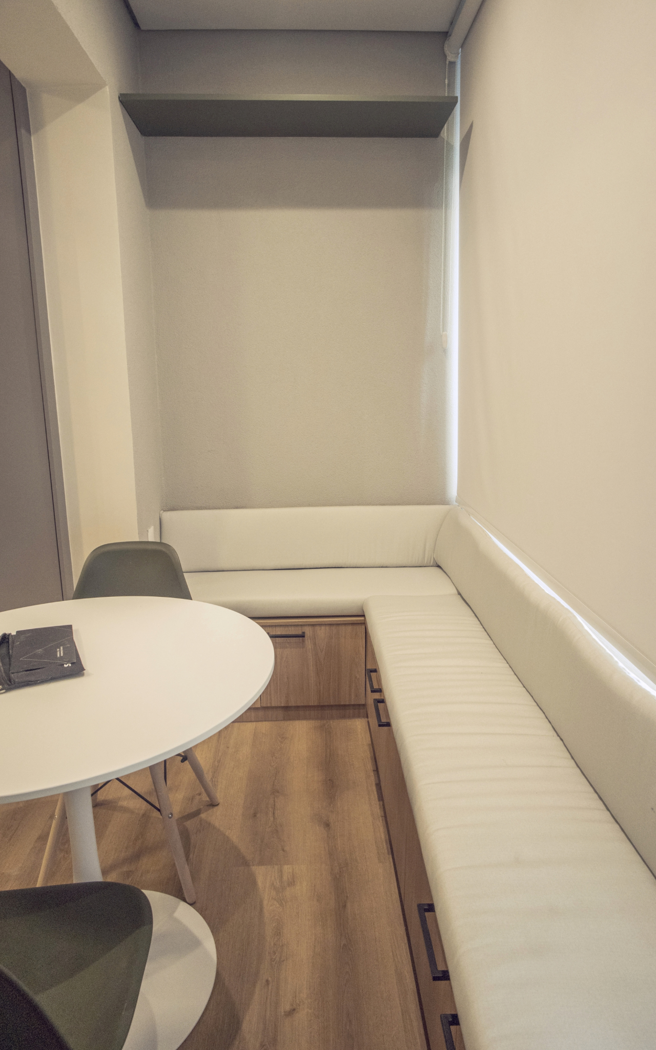 Obra pronta: Banco estofado branco em L junto à janela, com mesa redonda e cadeira