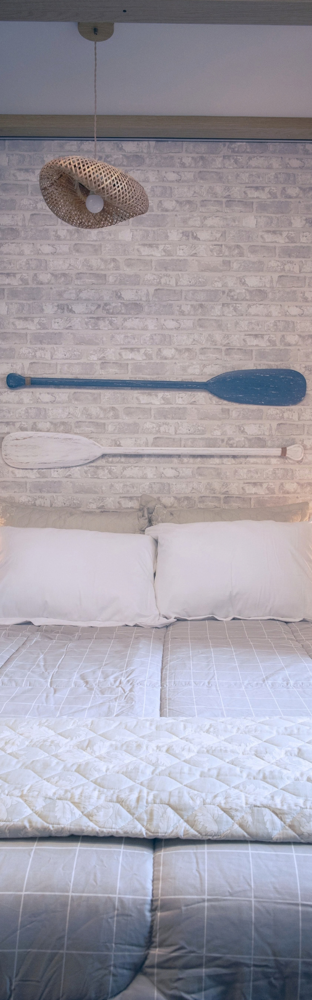 Obra pronta: Cama de casal diante de parede de tijolinho branco com remos decorativos e pendente de palha