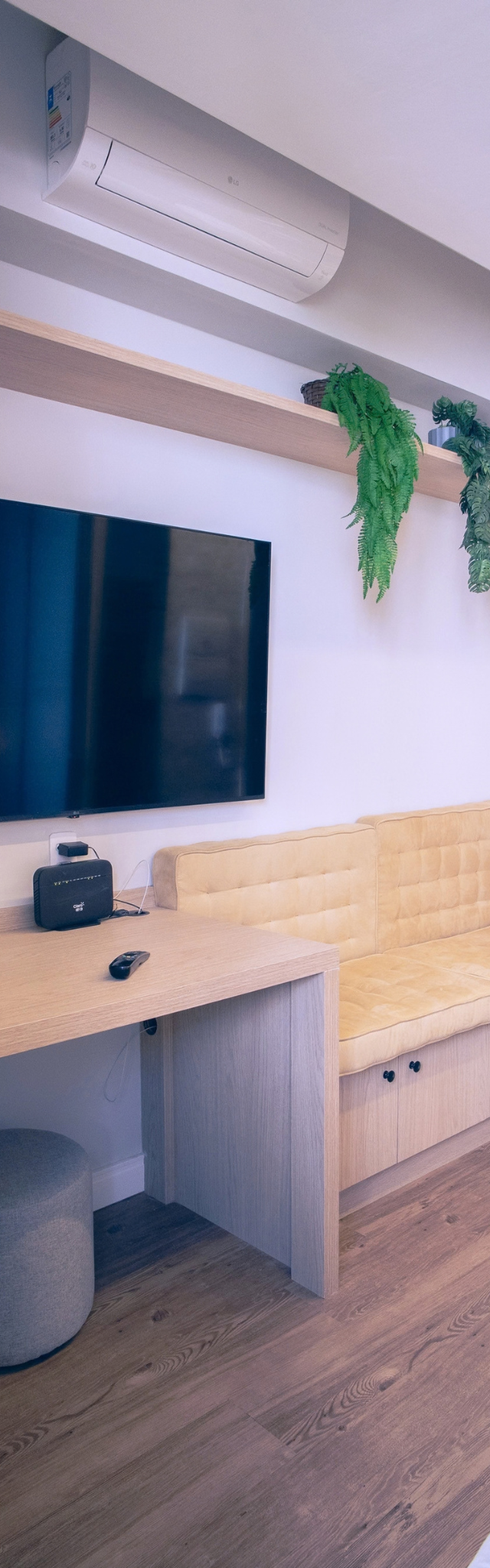 Obra pronta: Mesa de trabalho com cadeira e pufe, TV na parede, banco estofado amarelo e plantas na prateleira