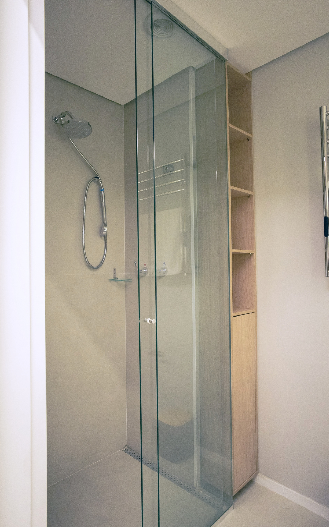 Obra pronta: Box de vidro com ducha, revestimento cinza claro e nichos de madeira ao lado