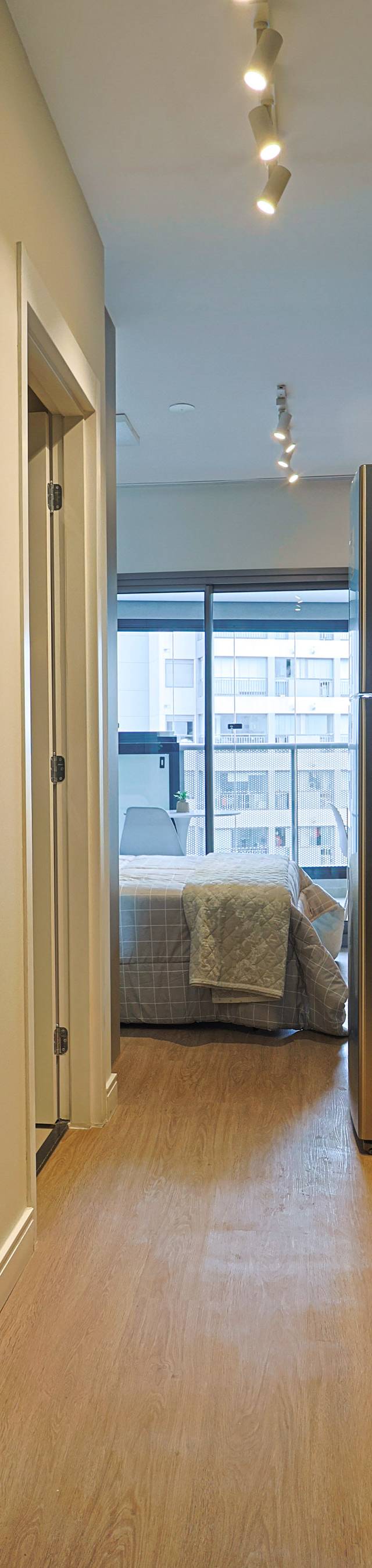 Obra pronta: Entrada do studio com cozinha de bancada escura, nicho de madeira iluminado e cama ao fundo