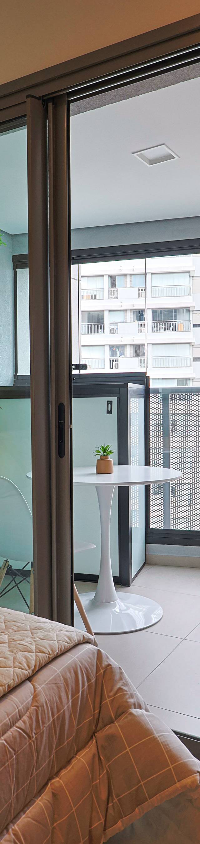 Obra pronta: Varanda com jardim vertical, mesa redonda branca e vista de prédios, vista da cama