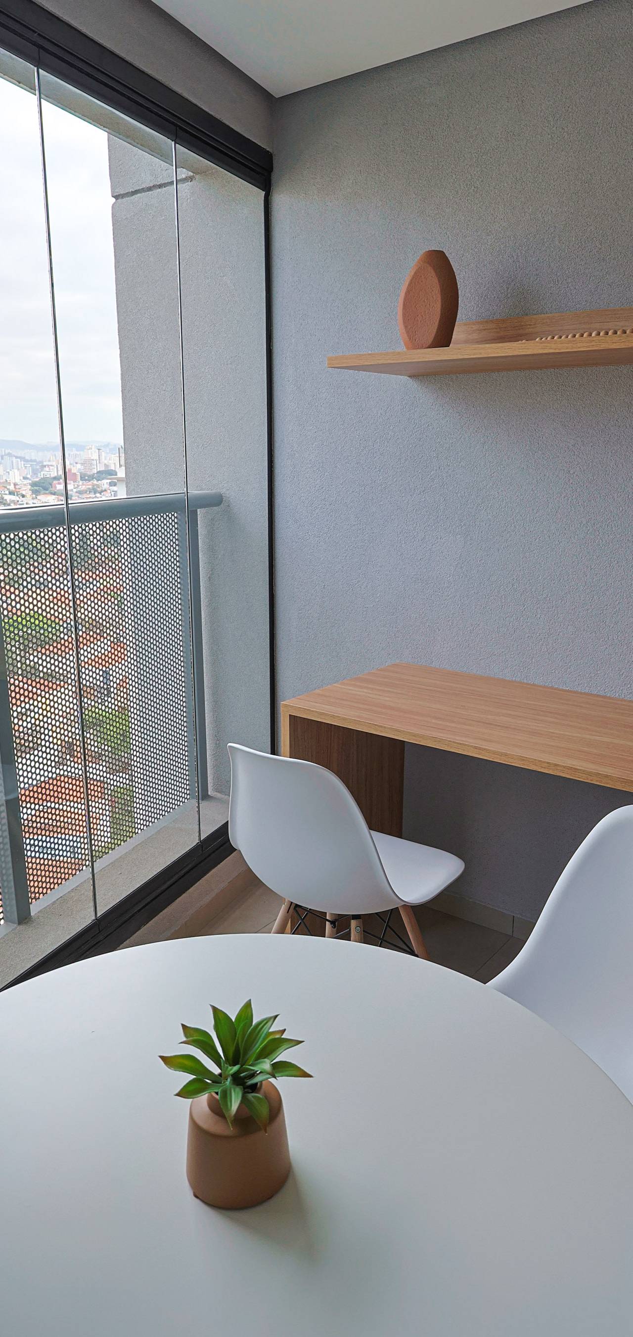 Obra pronta: Varanda envidraçada com mesa redonda, cadeiras brancas, bancada de madeira e vista da cidade