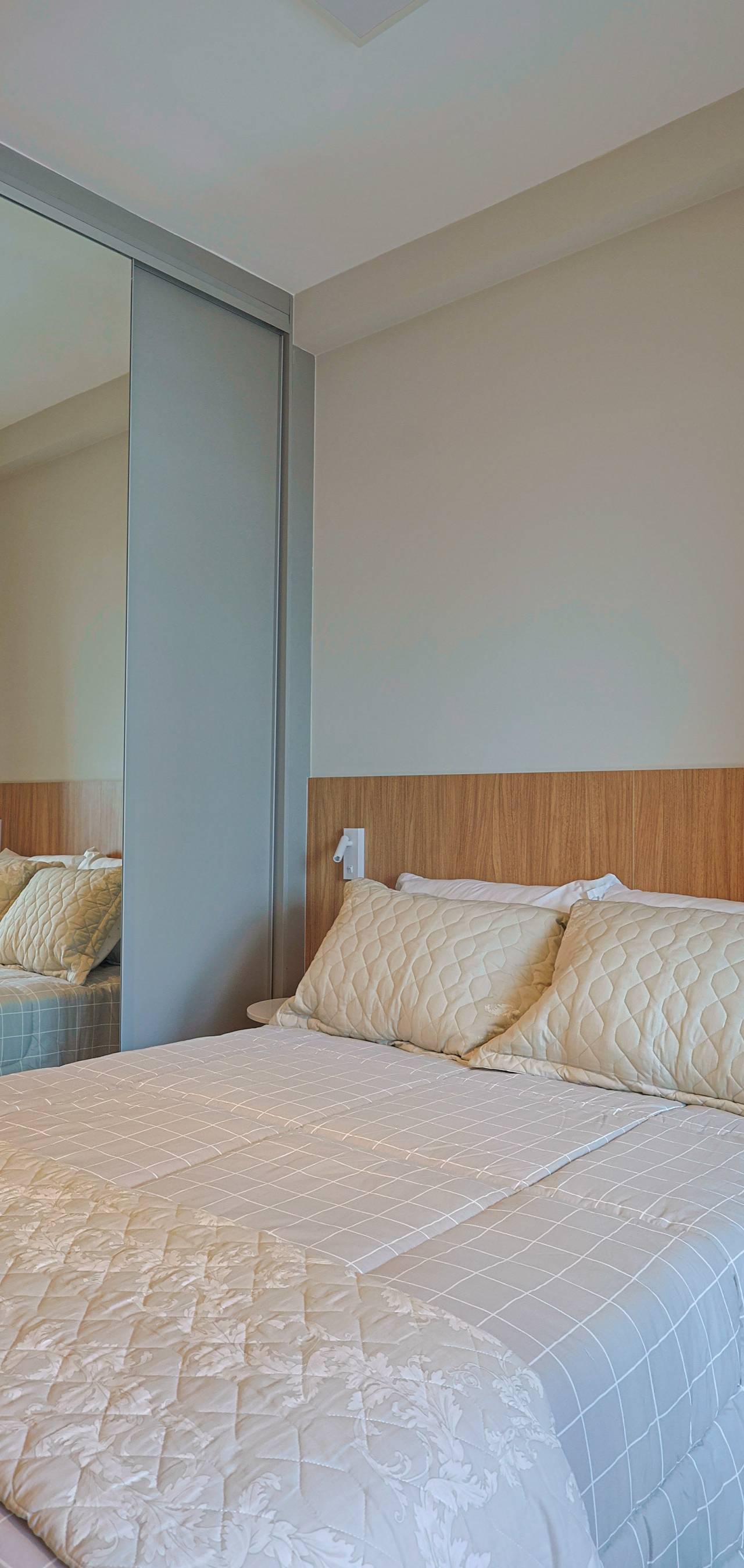 Obra pronta: Cama de casal com almofadas claras, cabeceira de madeira e armário espelhado