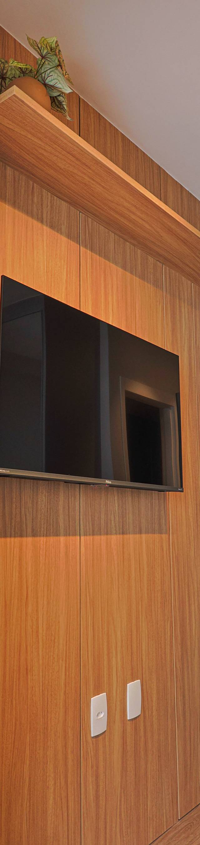 Obra pronta: Painel de madeira com TV e prateleira, ao lado de estante curva com objetos decorativos