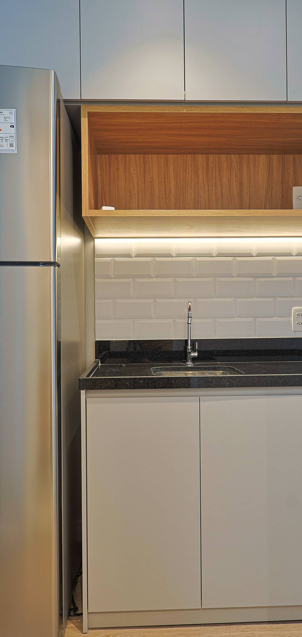 Obra pronta: Cozinha com geladeira inox, bancada de granito preto, cuba e nicho de madeira iluminado