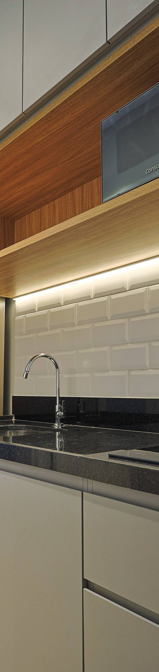 Obra pronta: Cozinha com micro-ondas no nicho de madeira iluminado, cooktop e bancada de granito preto