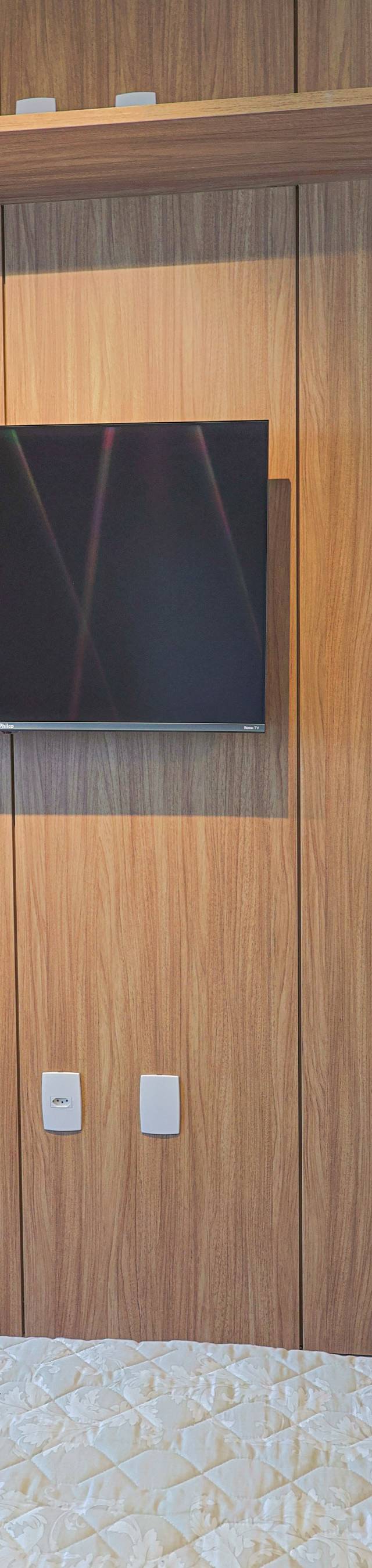 Obra pronta: Painel de madeira com TV e prateleira ao pé da cama, com estante curva ao lado