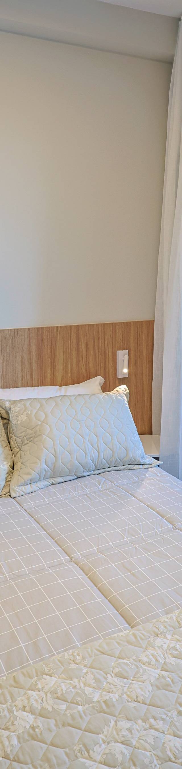 Obra pronta: Cama de casal com almofadas claras junto à porta de vidro e ao jardim vertical da varanda